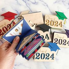 a hand is holding an open book with graduation caps and diplomas on it in front of a marble background