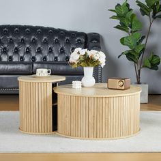 two tables with vases and flowers on them in front of a black leather couch