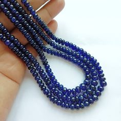 a hand holding three strands of dark blue glass bead necklaces on white background