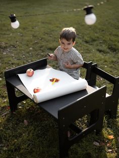 a little boy sitting in a chair with an apple on top of it and some string lights around him