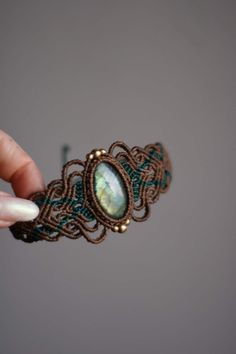 a hand holding a piece of wire with a stone in the middle and green beads around it