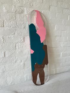 a skateboard that is sitting on a table next to a white brick wall with pink, blue and brown shapes