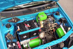 the engine compartment of a blue car with its hood open and several batteries in it