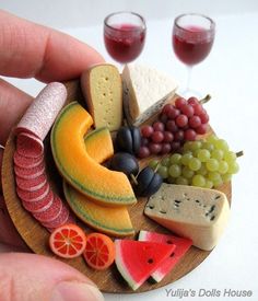 a person holding a miniature plate with fruit and cheese on it