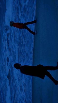 two people standing on the beach at night with their feet in the water and one person holding a surfboard