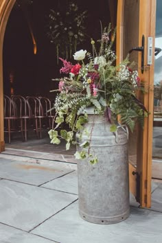 a large metal bucket filled with flowers sitting on top of a stone floor next to an open door