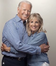 an older couple hugging each other in front of a white background with the man wearing a blue and white striped shirt