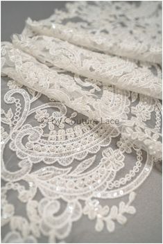 an image of white lace fabric with beads on it's edges and in the middle