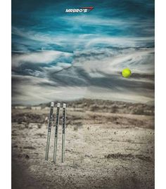 a yellow ball is in the air near two cricket bats on a dirt field with blue sky and clouds behind it