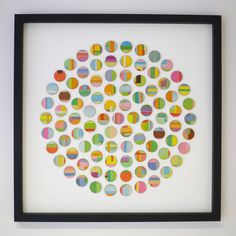 an art piece is displayed in a black frame on the wall, with multicolored circles arranged around it