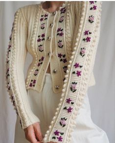 a woman wearing a white cardigan with pink flowers on the sleeves and buttons, standing in front of a white backdrop