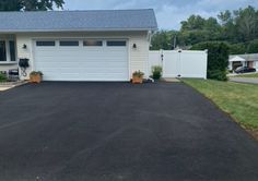 a driveway with two planters in front of it and a white fence around it