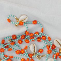 an orange and blue beaded necklace with seashells, pearls and beads on it