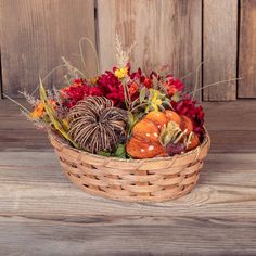 a basket filled with pumpkins and flowers on top of a wooden table