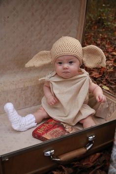 a baby sitting in an open suitcase wearing a hat and scarf on it's head