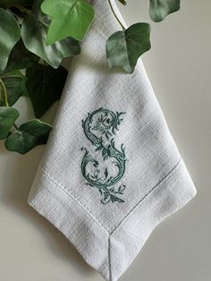 a white napkin with a green dragon embroidered on it next to some leaves and a potted plant