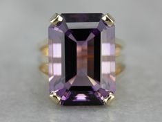 This amethyst cocktail ring features an outstanding amethyst straight from the source, we purchased it on one of our buying trips to Brazil. The play of light is outstanding and the depth of color is exquisitely filled with flashes of violet and raspberry! A perfect piece to celebrate any occasion from anniversary to birthday and everything in between!  Metal: 14K Yellow Gold  Gem: Amethyst 10.00 Carats (approximately)  Gem Measurements: 17.9 x 13 mm, Emerald Cut  Ring Size: 6 Marks: "14K JM" Stamped on the inside band Amethyst Cocktail Ring, Emerald Cut Ring, Purple Gems, Emerald Cut Rings, February Birthstone, February Birth Stone, The Source, Cocktail Ring, Eternity Bands