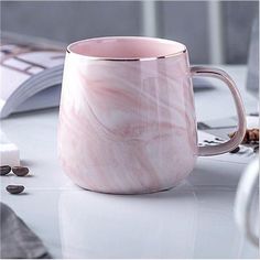 a pink marbled coffee mug sitting on top of a white table next to a keyboard