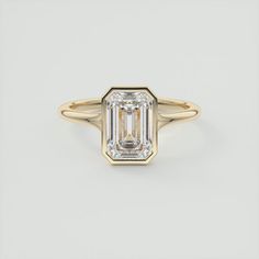 an emerald - cut diamond ring in yellow gold, set on a white background with the center stone partially surrounded by a thin band