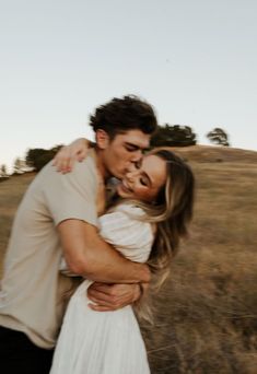 a man and woman are hugging in the field together, with one holding the other's head