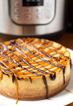 a cheesecake covered in caramel drizzle on a plate next to an instant pressure cooker