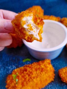 someone is dipping some food into a small white bowl with ranch dressing in it on a blue surface