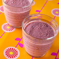 two glasses filled with pink smoothie sitting on top of a yellow table cloth next to each other