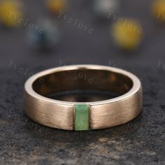 a gold wedding band with a green stone in the center on a black surface,