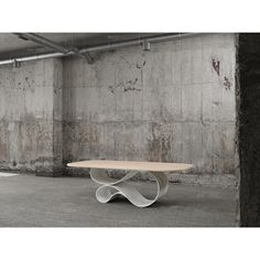 a white table in an empty room with concrete walls and exposed pipes on the ceiling