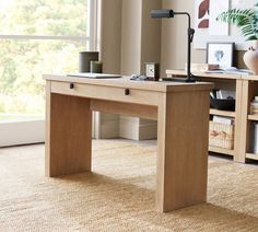 a wooden desk with a lamp on it in front of a window and bookshelf