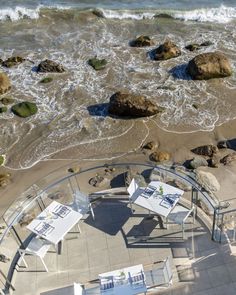 an aerial view of tables and chairs on the beach with waves crashing in to shore