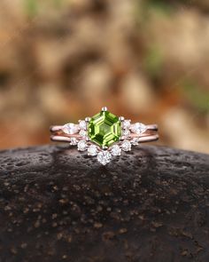 an engagement ring with a green tourmaline surrounded by white diamonds on top of a rock