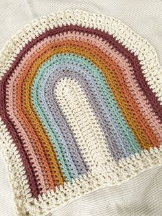 a multicolored crocheted rug on top of a white blanket with a rainbow in the middle