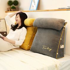 a woman sitting on a bed with pillows and a tablet in front of her face