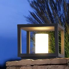 a light that is sitting on top of a stone wall next to some grass and trees