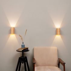 a chair sitting next to a table with a vase on it and two lights above it