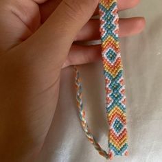 a hand is holding a bracelet made with multicolored seed stitchs and beads