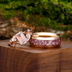 two wedding rings sitting on top of a wooden table in front of some rocks and trees