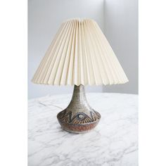 a lamp that is sitting on top of a white tablecloth with a beige shade