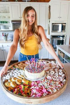 a woman standing in front of a tray filled with donuts and sprinkles