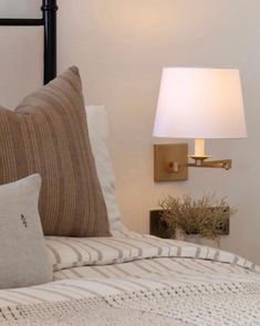 a bed with two pillows and a lamp on the wall next to it in a bedroom