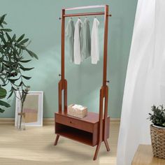 a wooden clothes rack with two shirts hanging on it's hangers and a plant in the corner