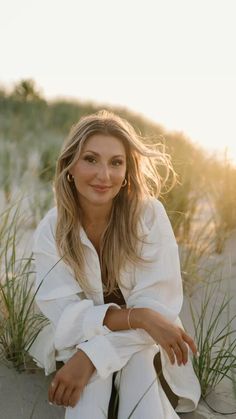 a woman sitting on top of a sandy beach next to tall grass and sand dunes