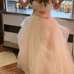 a woman standing in front of a counter wearing a pink dress and holding a drink