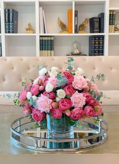 a vase filled with pink and white flowers sitting on top of a table next to a book shelf