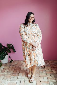 The Oakley Midi dress in a cream base with a peach and brown rose floral design is both stylish and functional. With a high neck, zipper in the back, and long sleeves with elastic cuffs, this dress is comfortable and easy to wear. The elastic waist with a tie creates a flattering silhouette, while the pleated bottom adds a touch of elegance. Model is wearing a small and is 5'8". Plus model is wearing a 2X and is 5'11". Size Chart Length Bust Waist S 47" 34" 32" M 47" 37" 34" L 47.5" 40" 36" XL 47.5" 44" 38" XXL 48" 48" 41" XXXL 48.5" 52" 44" *Measurements are approximate and are measured while hanging* Fabric and Care 100% Polyester Hand wash cold. Do not bleach. Lay flat to dry. Low iron if needed or dry clean. Cream Long Sleeve Midi Dress With Floral Print, Long Sleeve Cream Midi Dress With Floral Print, Long Sleeve Cream Floral Midi Dress, Peach Floral Print Long Sleeve Dresses, Peach Long Sleeve Floral Print Dress, Tiered Dresses, Plus Model, Teen Dress, Hanging Fabric