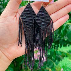 a pair of black beaded earrings with tassels in the palm of a person's hand