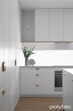 a kitchen with white cupboards and an oven next to a plant in a vase