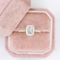 an engagement ring with a large emerald cut diamond in the center on a pink velvet box