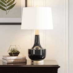 a table with a lamp on it and some books sitting next to it in front of a painting